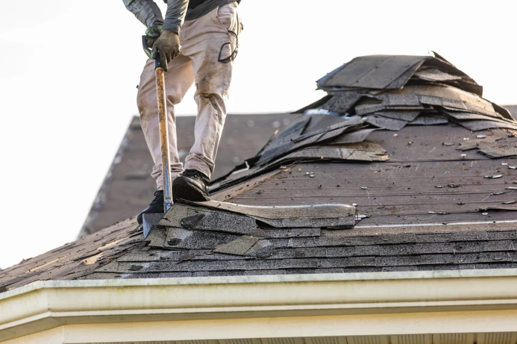 roof shingles get removed by roofing contractor with shovel