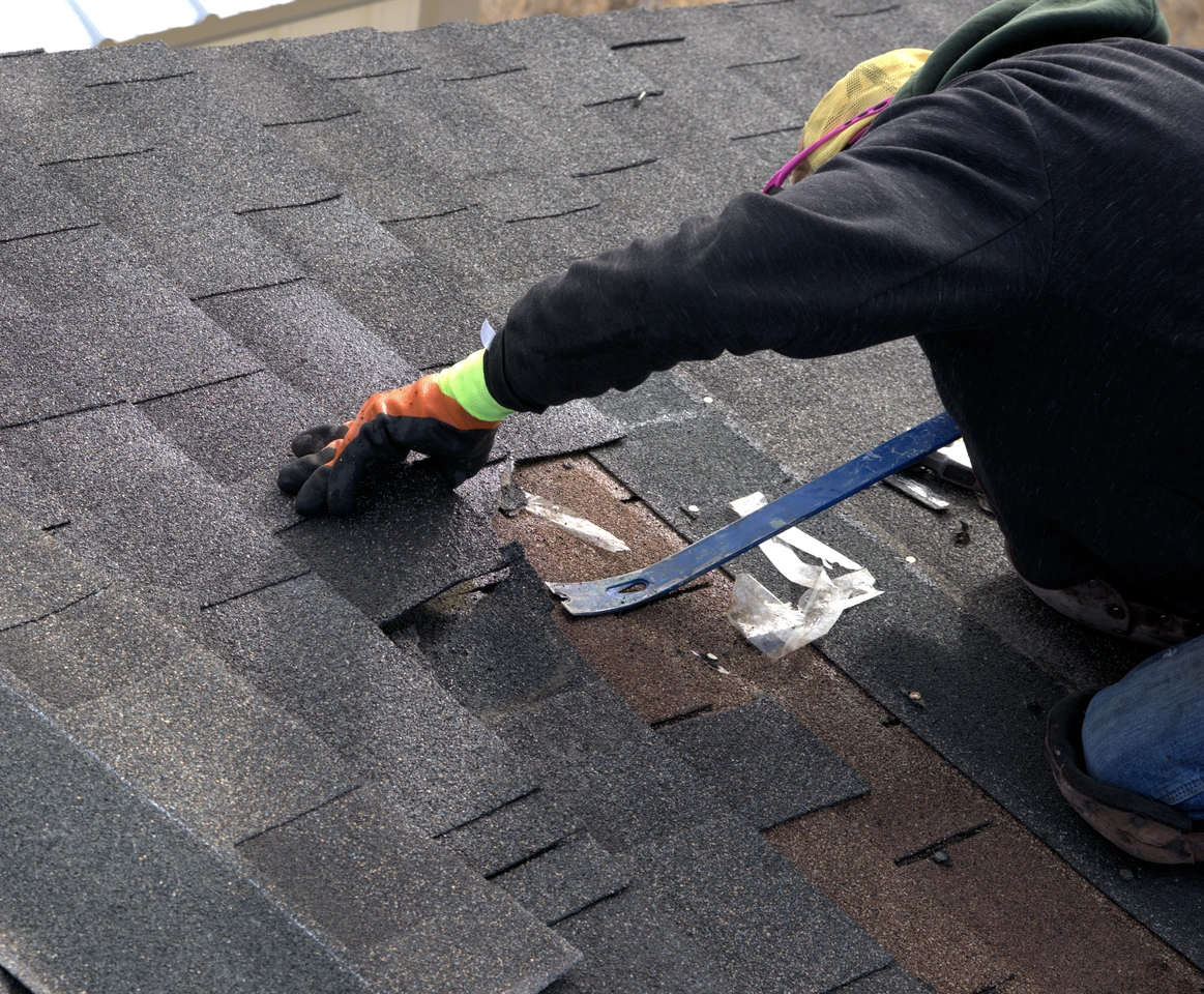 contractor using pry bar removes roof shingles